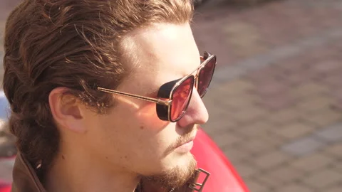 Loop video of curly young man in biker suit put on his red glasses and put's off Stock Footage 152790482