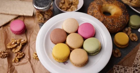 Looping rotating closeup of assorted macarons on plate with bagel and walnuts Stock Footage 320171053