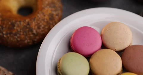 Looping tabletop closeup of colorful macarons with bagel and walnuts on plate Stock Footage 320165624