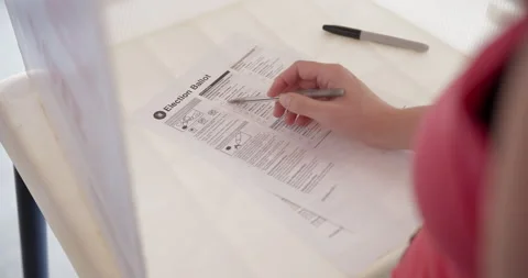 Loose OTS close up on woman's hand completing voting ballot Stock Footage 284264502