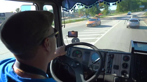 Lorry driver riding on city road at sunny day. Man in cap controlling his truck Stock Footage 296215448