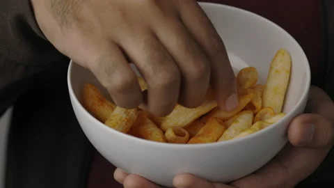 Lose up young man eating crispy penne pasta shaped salty snacks in bowl. Fast fo Stock Footage 152807196