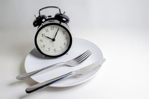Losing weight. A fork, knife with a clock on a white plate on a white backgro Stock Photos