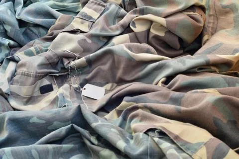 Lost and empty army dog tag lies on pile of folded camouflage clothes 写真素材