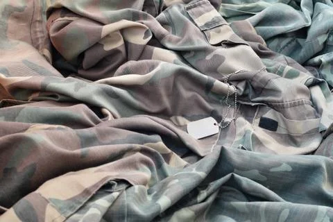 Lost and empty army dog tag lies on pile of folded camouflage clothes 写真素材