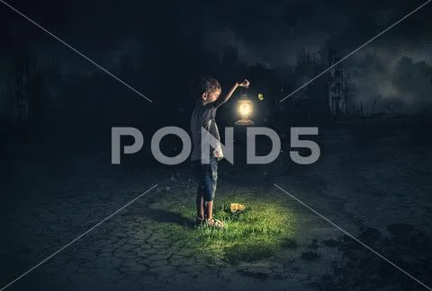Lost child holding an old lamp in an apocalyptic environment Stock Photos