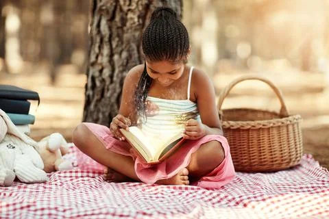 Lost in magical worlds. a little girl reading a book with her toys in the woods. Stock Photos
