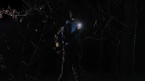 A lost man with a backpack walks through a dark forest at night, holding a Stock Footage 302725893