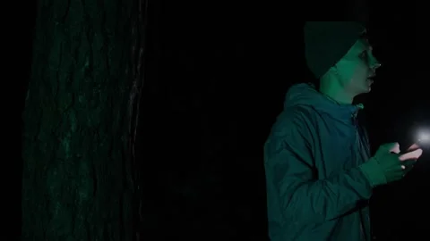 A lost man in a dark forest at night, holding a flashlight and looking around Stock Footage 302348178