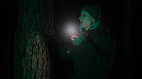 Lost man emerging from darkness in a forest at night, using a phone flashlight Stock Footage 303141409