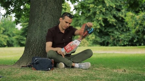 A lost man in sunglasses is trying to read a map in the park Stock Footage 73349510
