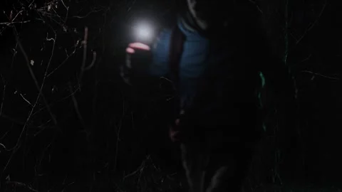 A lost man walks through a dark forest at night, holding a flashlight in one Stock Footage 300974812