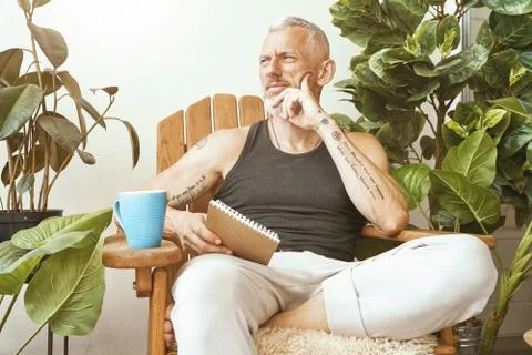 Lost in thoughts. Focused middle aged man sitting on the sunny terrace of his Stock Photos