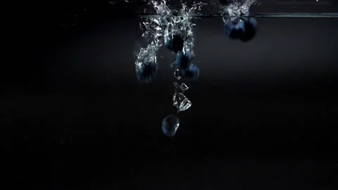 A lot of blue fresh blueberries fall into the water with splashes, slowly sinkin Stock Footage 133353777