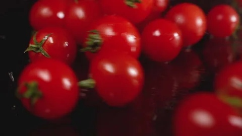A lot of cherry tomatoes fall into a puddle of water on a black background Stock Footage 136159939