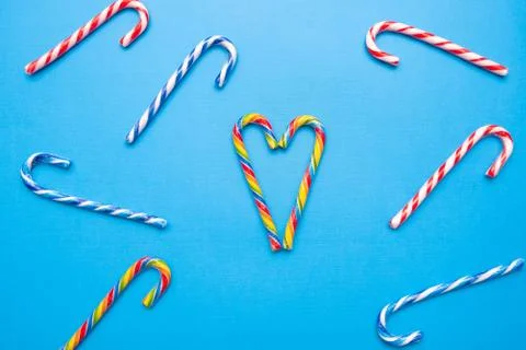 Lot of multi-colored candy canes and one heart on a blue background, copy space Stock Photos