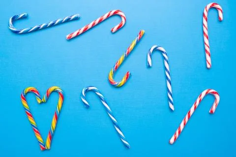 Lot of multi-colored candy canes and one heart on a blue background, copy space Stock Photos