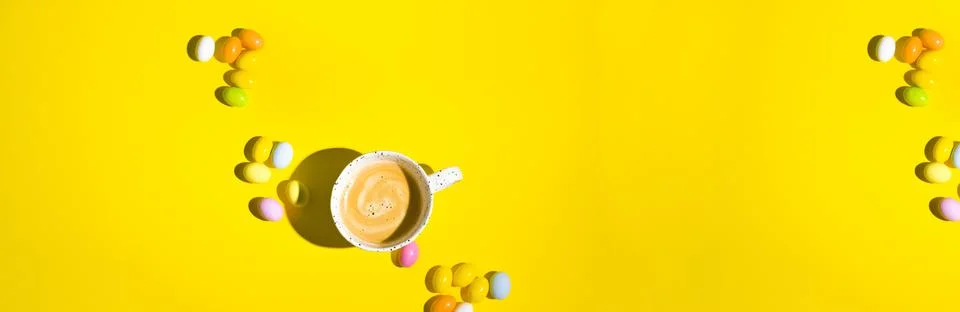 A lot of multi-colored Easter eggs and a mug of coffee with froth on a yellow Stock Photos