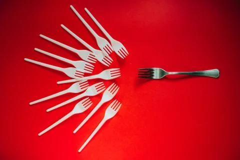 A lot of plastic forks and one metal on a red background. Stock Photos