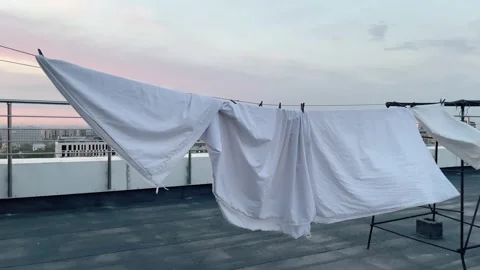 A lot of white sheets are dried in the sun rope on the roof top. Sunset. High Stock Footage 239299333