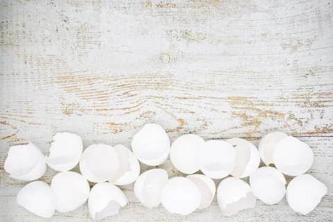 Lots of broken white eggshells on a light wooden background. Copy space 스톡 사진