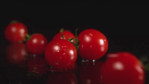 Lots of cherry tomatoes fall on the water with splashes on a black background Stock Footage 142196800