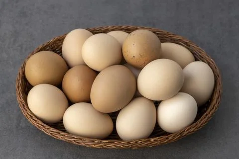 Lots of chicken eggs in a wooden basket on a gray background. Stock Photos