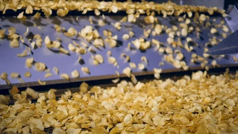 Lots of fried crisps fall from metal conveyor at a food production factory, slow Stock Footage 105595602