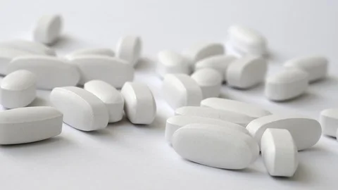 Lots of large white oval tablets fall and scatter on surface. Video stock 108673224