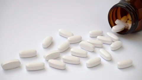 Lots of large white oval tablets lie near a brown glass bottle. Video stock 108692144