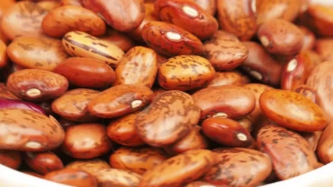 Lots of raw brown beans are spinning in a white plate close-up Stock Footage 166968676