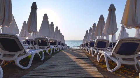 Lots of sun loungers in the rays of the setting sun, lowered sunshades, a path Stock Footage 272761253