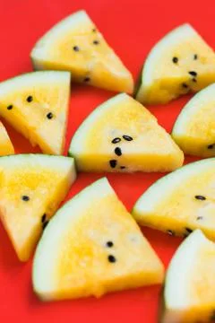 A lots of triangular pieces of ripe yellow watermelon on red background Stock Photos
