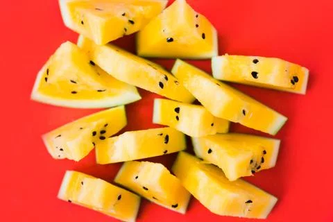 A lots of triangular pieces of ripe yellow watermelon on red background 스톡 사진