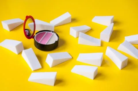 Lots of white triangular sponges and lip gloss on a yellow background Stock Photos