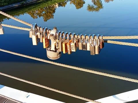 Love locks on bridge railing over calm river Stock Photos
