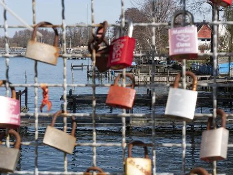 Love locks hang on a grid, in the background is a lake with a marina Stock Photos