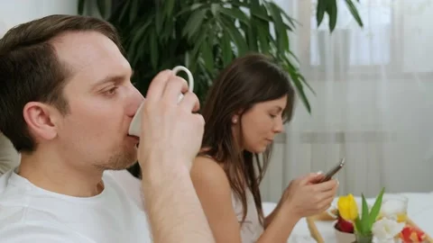 Lovely attractive couple using mobile phone during breakfast in the bed, lying Stock Footage 156329888