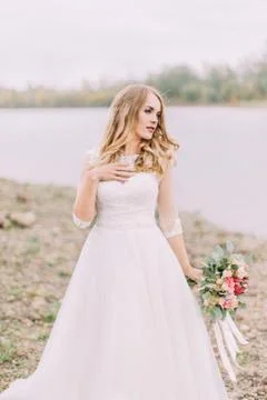 The lovely bride is posing while looking aside. The wedding bouquet in the hand. Stock Photos