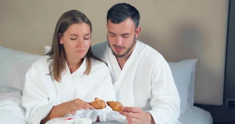 Lovely couple eats croissants having breakfast on large bed Video stock 141051920