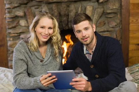 Lovely couple using tablet PC in front of lit fireplace Stock Photos