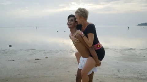 Lovely gay couple on piggyback ride at the beach. Stock Photo