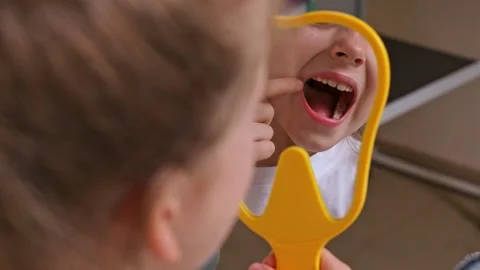 Lovely little girl looking in the mirror at her teeth after teeth surgery  Stock Footage 307457953