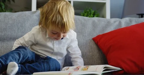 Lovely small boy sitting on the grey sofa and reading the book in the Stock Footage 82917479