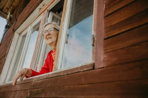 Lovely, smiling grandmother watching out of the window and enjoying sunny day, a Stock Photos