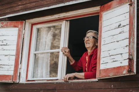 Lovely, smiling grandmother watching out of the window and enjoying sunny day, a Stock Photos