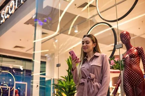 Lovely smiling lady using mobile phone at window store shop center, enjoying  Stock-Fotos