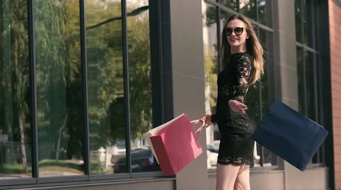 Lovely young woman turns around holding shopping bags on window background Stock Footage