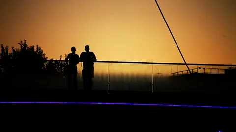 Lovers Couple and Jogging Woman on Bridge Back Lit Silhouette at Sunset Stock Footage