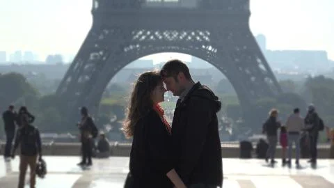 Lovers embrace in front of Eiffel tower, people passing Stock Photos